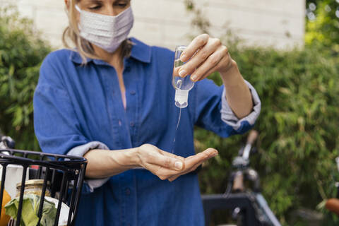 Woman with bicycle wearing face mask disinfecting her hands stock photo