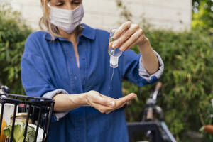 Woman with bicycle wearing face mask disinfecting her hands - MFF05737