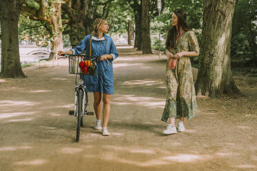 Two women with bicycle and face mask walking in park - MFF05749