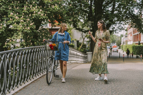 Zwei Frauen mit Fahrrad und Gesichtsmaske gehen auf einer Brücke - MFF05752
