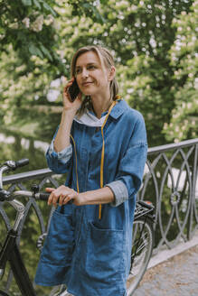 Frau auf einer Brücke mit Gesichtsmaske und Fahrrad beim Telefonieren - MFF05753