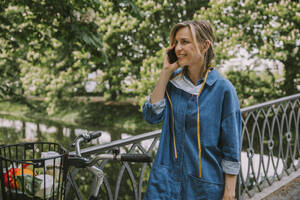 Woman on a bridge with face mask and bicycle talking on the phone - MFF05754