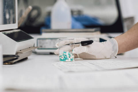 Nahaufnahme einer Technikerin, die einen Becher mit Tabletten auf dem Schreibtisch eines Labors hält, lizenzfreies Stockfoto