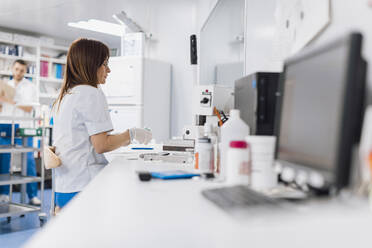 Female scientist sitting at desk while doing research in laboratory - OCAF00510