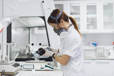 Arzt gießt eine Chemikalie in ein Becherglas auf einer Waage, während er im Labor forscht - OCAF00512