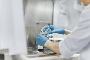 Junger männlicher Techniker gießt eine Chemikalie aus einem Becher, während er im Labor forscht - OCAF00516