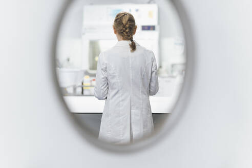 Senior female scientist seen through window at laboratory, rear view - OCAF00529