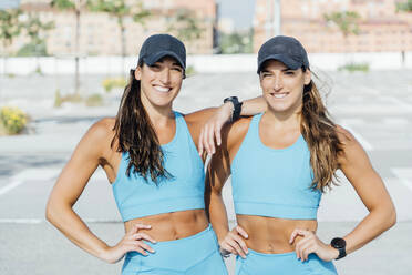 Porträt von lächelnden selbstbewussten jungen Zwillingsschwestern in Sportkleidung, die an einem sonnigen Tag im Freien stehen - OCMF01307