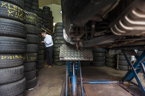 Senior male entrepreneur standing by tire stacks at store - DIGF11545