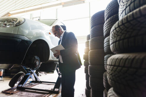 Senior businessman holding digital tablet while examining car wheel at store - DIGF11548