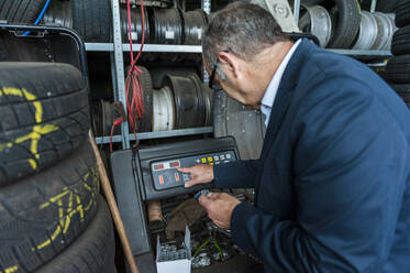 Senior male entrepreneur using machinery by tires at store - DIGF11559