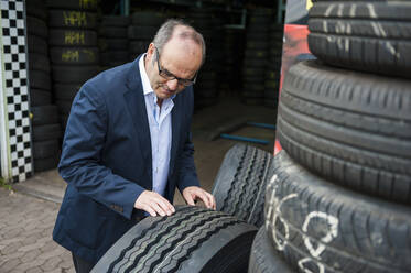 Senior male owner checking rubber tire at store - DIGF11560