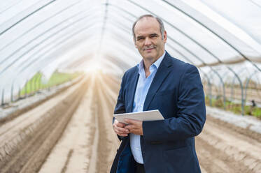 Portrait of confident businessman holding digital tablet while standing at greenhouse - DIGF11573