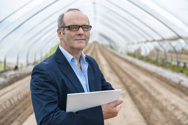 Confident senior businessman holding digital tablet while standing at greenhouse - DIGF11574