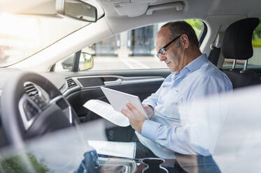 Geschäftsmann, der ein digitales Tablet benutzt, während er im Auto sitzt - DIGF11575