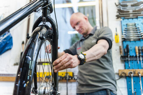 Fahrradmechaniker bei der Arbeit in einer Fahrradwerkstatt, Überprüfung des Vorderrads - DIGF11587