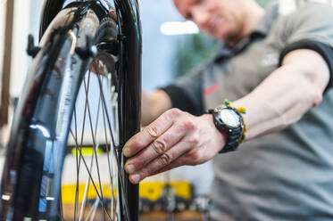 Bicycle mechanic working in bike shop, checking front wheel - DIGF11588