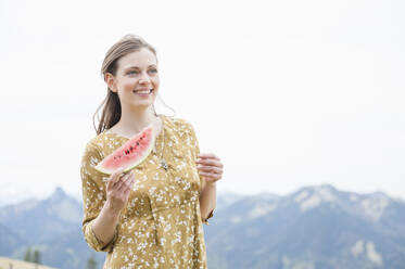 Beautiful smiling woman holding watermelon slice while standing against sky - DIGF11620