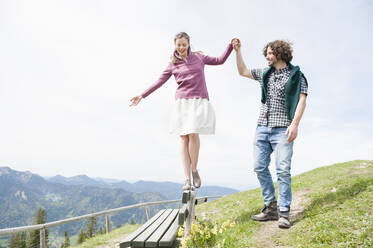 Lächelnder Mann, der die Hand einer Frau hält, die auf einer Bank in den Bergen spazieren geht, bei klarem Himmel - DIGF11631