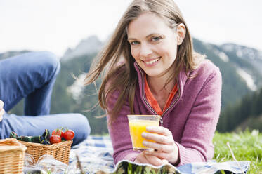 Porträt einer lächelnden Frau, die einen Saft in der Hand hält, während ein Mann beim Picknick liegt - DIGF11641