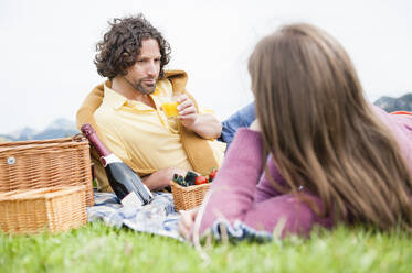 Gut aussehender Mann trinkt Saft, während er sich zurücklehnt und eine Frau beim Picknick ansieht - DIGF11642