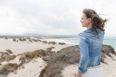 Glückliche Frau mit wehenden Haaren steht in den Dünen und genießt die Aussicht, Sardinien, Italien - DIGF11682