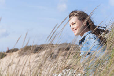 Portrait of happy woman with blowing hair sitting in dunes, Sardinia, Italy - DIGF11686