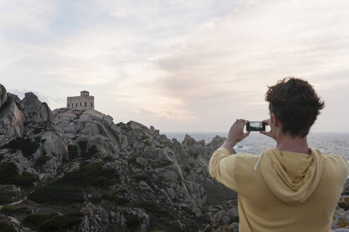 Back view of tourist taking photo of lighthouse, Capo Testa, Sardinia, Italy - DIGF11693