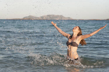 Glückliche Frau im Bikini steht im Meer und spritzt mit Wasser, Sardinien, Italien - DIGF11713