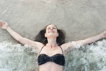 Porträt einer glücklichen Frau im Bikini, die am Meeresufer liegt und die Brandung genießt, Sardinien, Italien - DIGF11716