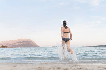 Teenage girls wearing a pink bikini running along a sandy beach by a lake.  stock photo