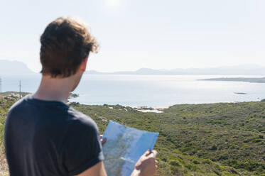 Back view of man with map looking at view, Sardinia, Italy - DIGF11727