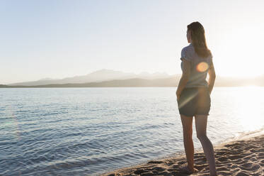 Back view of woman standing at seashore by sunset looking at view, Sardinia, Italy - DIGF11729