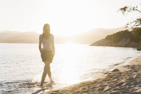 Rückenansicht einer Frau, die bei Sonnenuntergang am Meeresufer watet, Sardinien, Italien - DIGF11730