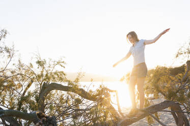 Frau balanciert bei Sonnenuntergang auf einem Baumstamm, Sardinien, Italien - DIGF11732