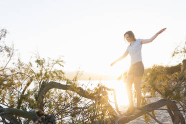 Woman balancing on tree trunk by sunset, Sardinia, Italy - DIGF11732