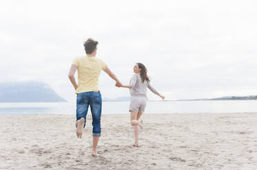 Happy couple running hand in hand on the beach, Sardinia, Italy - DIGF11739