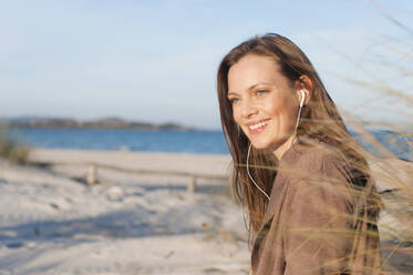 Portrait of smiling woman on the beach listening music with earphones, Sardinia, Italy - DIGF11764