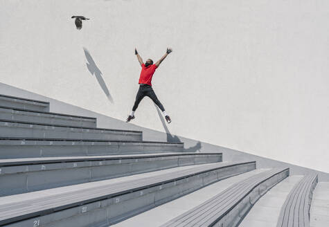 Sportler mit Gesichtsmaske springt auf Treppe mit fliegendem Vogel - AHSF02629