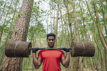 Sportsman exercising with wooden barbells in the forest - AHSF02653