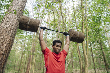 Sportsman exercising with wooden barbells in the forest - AHSF02654