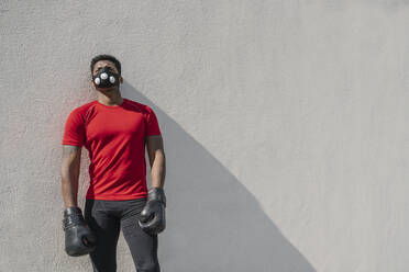Porträt eines Sportlers mit Gesichtsmaske und Boxhandschuhen an einer Wand - AHSF02678