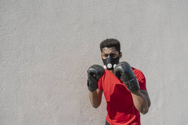 Porträt eines Sportlers mit Gesichtsmaske und Boxhandschuhen an einer Wand - AHSF02679