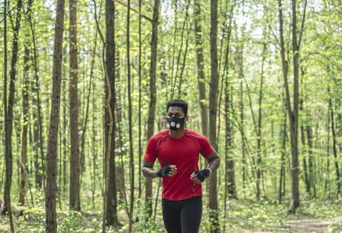 Sportler mit Gesichtsmaske beim Laufen im Wald, lizenzfreies Stockfoto