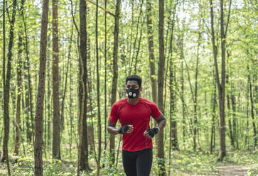 Sportsman wearing face mask running in the forest - AHSF02696
