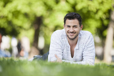 Portrait of smiling young man lying on blanket in park - DIGF11786