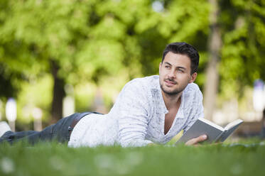 Junger Mann liest auf einer Decke im Park liegend ein Buch - DIGF11787