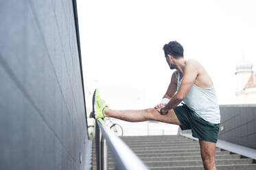 Young man stretching his leg on railing in the city - DIGF11793