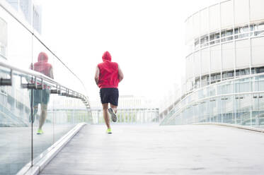 Rear view of young man jogging on footbridge in the city - DIGF11796