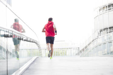 Rear view of young man jogging on footbridge in the city - DIGF11797